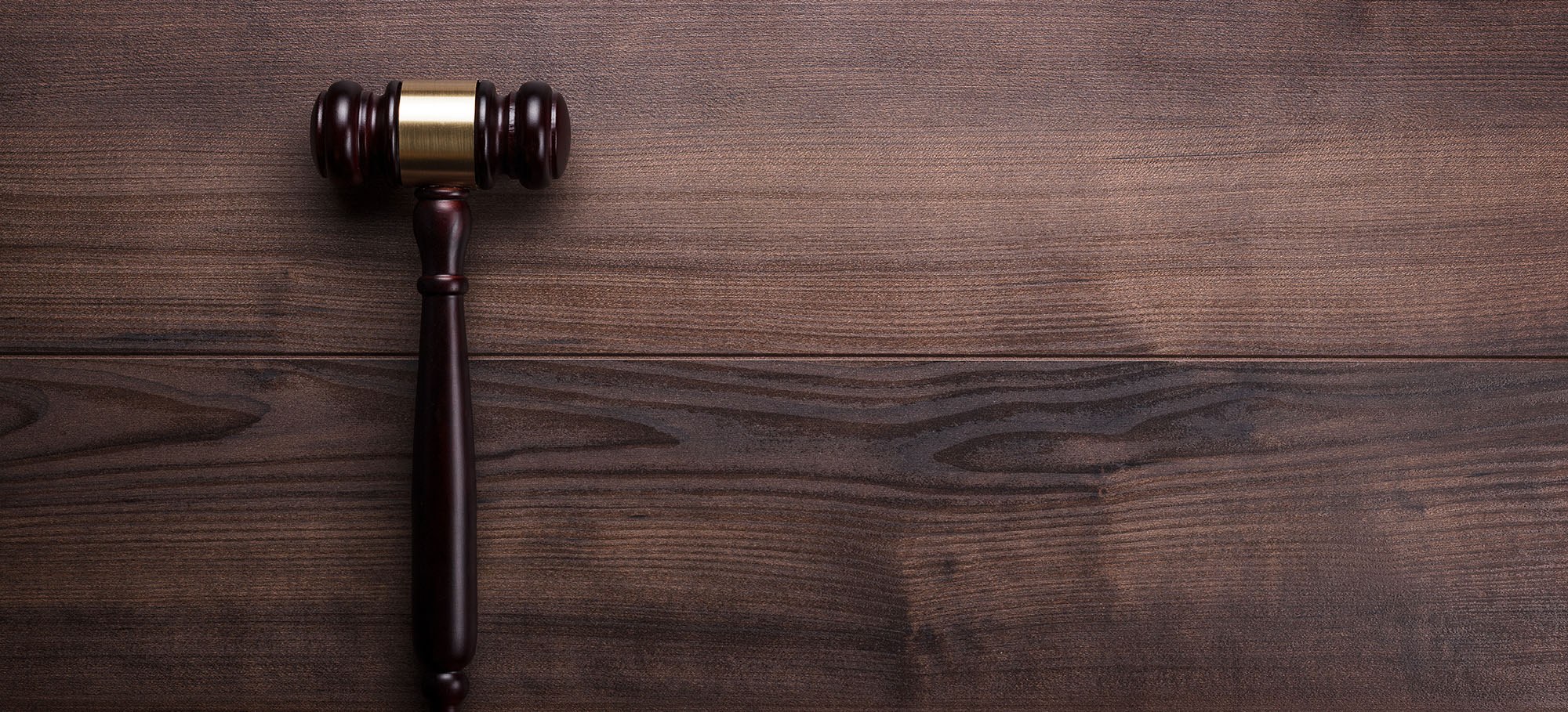 Wooden gavel with a golden ring between the mallets sitting on a wooden table.